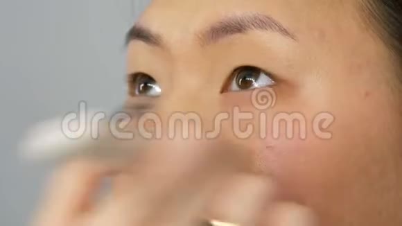 专业化妆师将粉底遮瑕或荧光粉涂在亚洲韩国模特的脸上并用特殊的刷子视频的预览图
