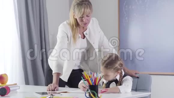 自信的白种人中年家庭教师站在女学生旁边写在练习本上的肖像中老年人视频的预览图