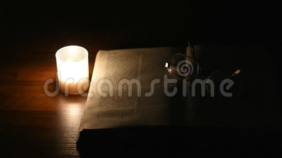 一支孤独的蜡烛在夜晚的桌子上闪烁在一本开放的书面前视频的预览图