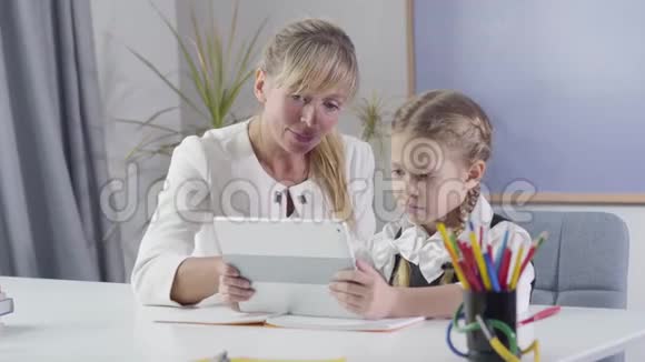 白种人中年妇女和小女学生坐在桌旁与平板电脑的肖像教师教学视频的预览图