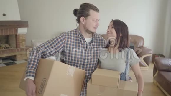 白种人夫妇站在客厅里拿着纸板箱微笑的肖像快乐的年轻家庭搬家视频的预览图
