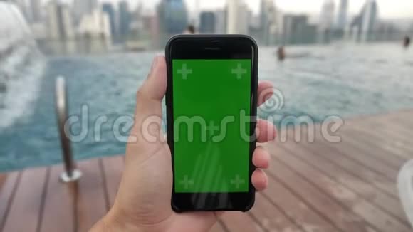 智能手机的特写镜头绿色屏幕彩色键放在游泳池附近在触摸屏上观看视频并跟踪视频的预览图