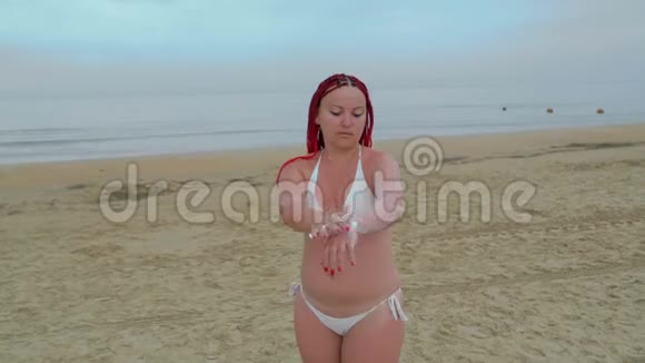 一位身穿白色泳衣的年轻女子在海滨涂防晒霜视频的预览图