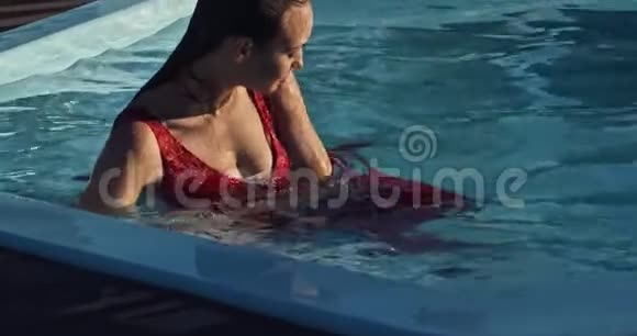 穿着红裙子的性感女人坐在游泳池里脸上带着微笑转过身来视频的预览图