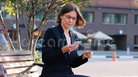 年轻的商务女性在户外支付wtith信用卡和她的手机网上付款视频的预览图