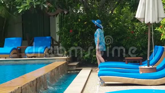 穿着蓝色泳衣戴着帽子戴着太阳镜的漂亮女士在游泳池里躺着一个阳光休息室里面有清澈的水视频的预览图