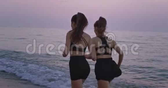 晚上两位女士穿着黑色运动服在海滩上奔跑从后面拍视频视频的预览图
