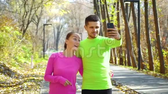 一对迷人的运动员使用智能手机从秋季公园现场直播视频的预览图