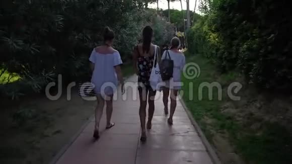 年轻的女士们沿着马路走过绿色公园的夹竹桃视频的预览图