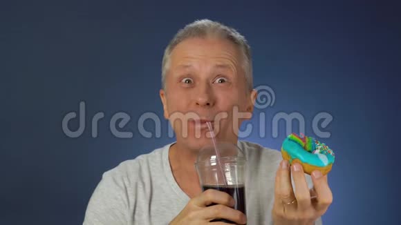 有趣的中年男人滑稽地吃着蛋糕用吸管把他的碳酸饮料从一个大玻璃杯里洗下来视频的预览图