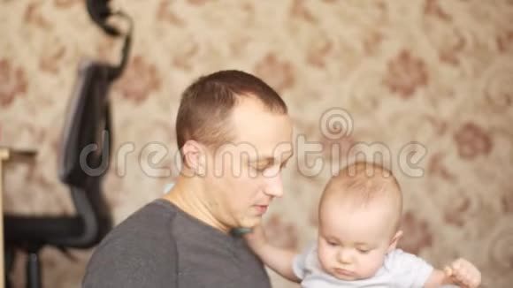 父亲坐在地板上手里拿着他的孩子和他的儿子玩耍亲吻他他们都很高兴视频的预览图