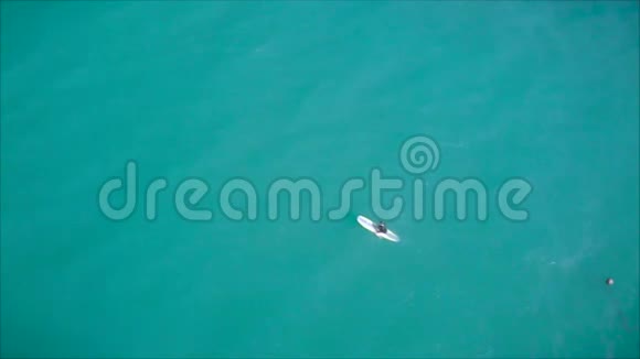 一位年轻的女冲浪者躺在冲浪板上双手划向海浪这位冲浪者是空中摄影的顶角视频的预览图