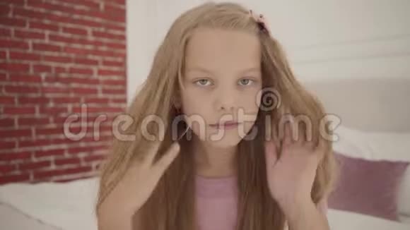 可爱的白人女孩灰色的眼睛和金发坐在卧室里固定她的头发打开鲜红的头发视频的预览图