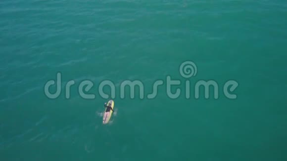 一位年轻的女冲浪者躺在冲浪板上双手划向海浪这位冲浪者是空中摄影的顶角视频的预览图