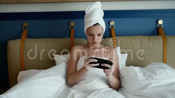 美丽性感的年轻女人洗澡后躺在床上玩手机游戏视频的预览图