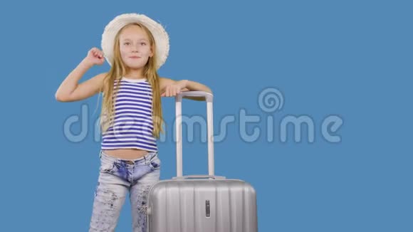 旅行女孩带着手提箱打招呼在演播室的蓝色背景上打招呼带手提箱的少女视频的预览图