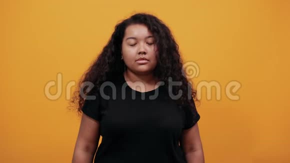 严肃的美国黑人妇女在橙色的墙上对着镜头露出三根手指视频的预览图