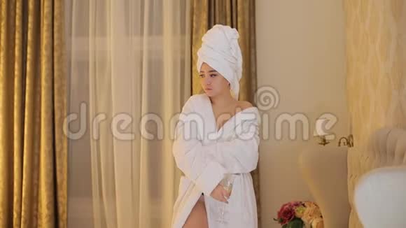 一个穿着白色浴袍和头上一条毛巾的有钱女孩在卧室里摆姿势视频的预览图
