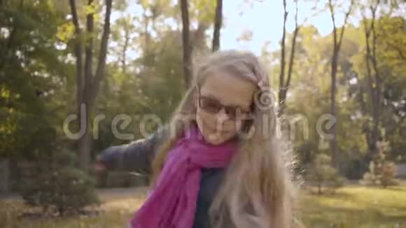 秋天公园拍摄的一个长着金色卷发的白人少女的肖像视频的预览图
