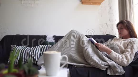 平静的女孩在沙发上看书躲在毯子里假期秋季或冬季休息视频的预览图