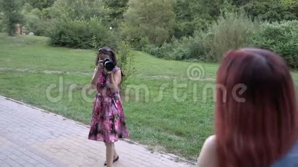 专业摄影师女人在露天拍摄一个年轻女孩模特的照片在公园日落她视频的预览图
