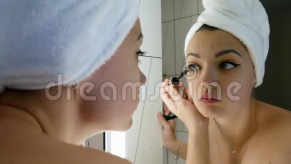 美丽的女人头上戴着毛巾化妆在镜子前画眼睛和彩色睫毛视频的预览图