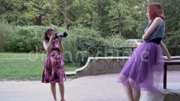 女摄影师在户外拍摄一个年轻女孩模特日落时在公园里她拿着一个带有摄象机的照相机视频的预览图