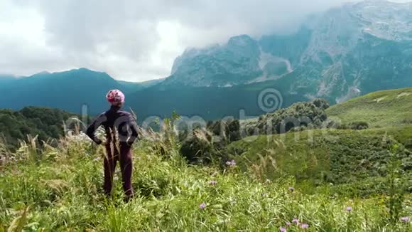 女徒步旅行者在山上欣赏美丽的风景和周围的野生自然岩石峭壁上的高山草甸视频的预览图