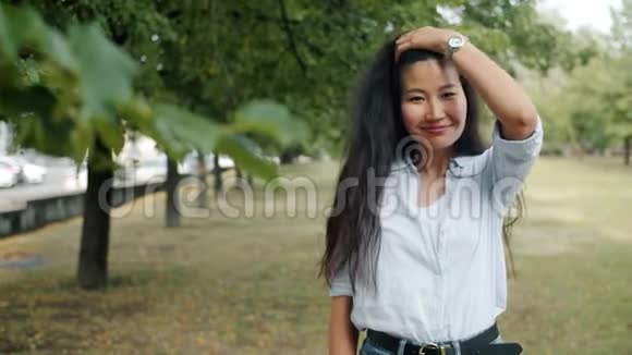 城市公园里迷人的亚洲女士微笑着抚摸头发的肖像视频的预览图