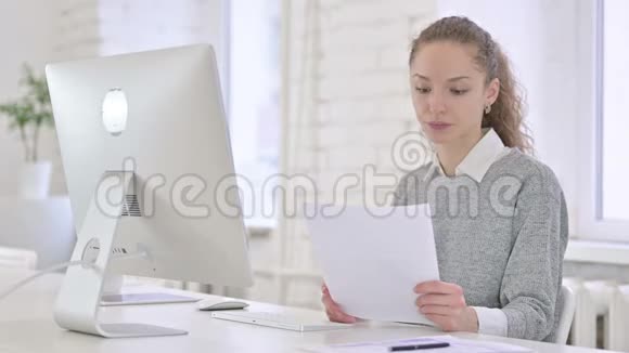 年轻的拉丁妇女阅读文件思考和工作在台式计算机视频的预览图