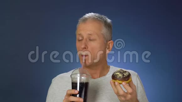 一个身材苗条的中年男人很高兴地吃蛋糕用吸管从一个大杯子里喝一杯碳酸饮料视频的预览图