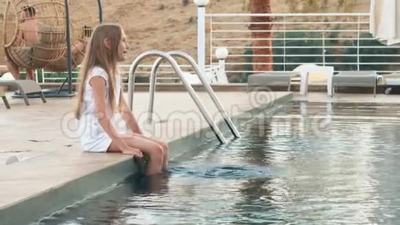 十几岁的女孩坐在游泳池边蘸水的腿快乐的女孩享受夏天的游泳池水视频的预览图