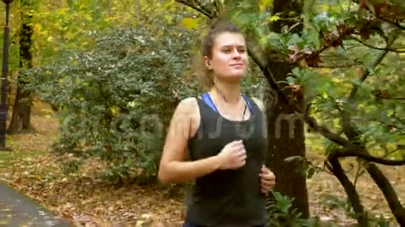 带着耳机的运动女孩在秋天公园慢跑视频的预览图