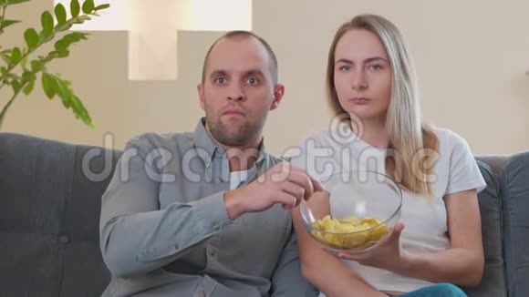 一对夫妇一边吃零食一边在沙发上看恐怖电影视频的预览图