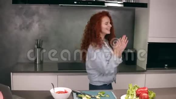 快乐活泼的红头年轻女子拿着勺子当麦克风在厨房里唱歌跳舞视频的预览图