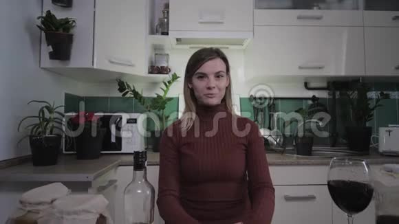年轻迷人的家庭主妇在家里的厨房里为她的博客写视频食谱并举起一杯葡萄酒女性vlog视频的预览图