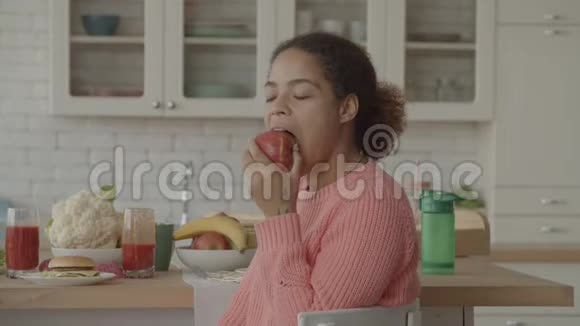 微笑的非洲女人在厨房里吃多汁的苹果视频的预览图