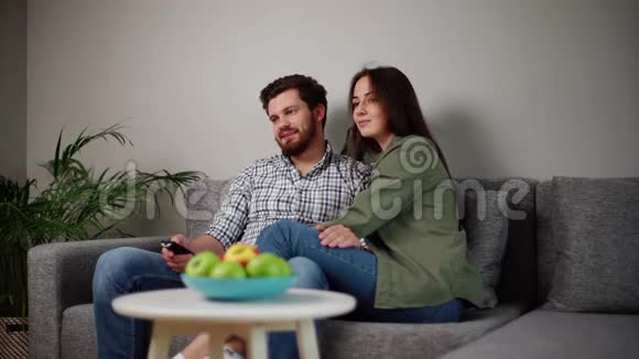 可爱的幸福夫妇正坐在柔软的沙发上在家看电视视频的预览图