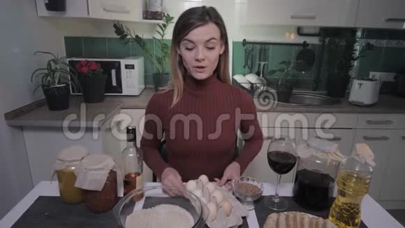 女性vlog年轻迷人的微笑女人在家里的厨房里为她的博客讲述视频食谱并举起一杯酒视频的预览图
