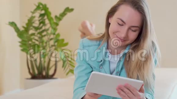 美丽的年轻女子在床上使用数码平板电脑视频的预览图