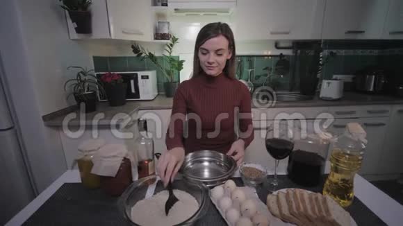 开朗的家庭主妇年轻漂亮的有趣的女人在厨房里坐在桌子上有烹饪的产品喝来自视频的预览图