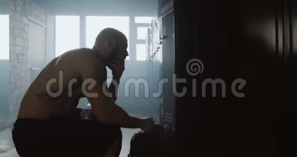 年轻的运动赤膊白种人男子独自坐在黑暗的健身房更衣室休息后锻炼克服困难视频的预览图