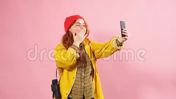 一个穿着黄色雨衣的旅游女孩在智能手机上给朋友吹了个吻的工作室肖像视频的预览图