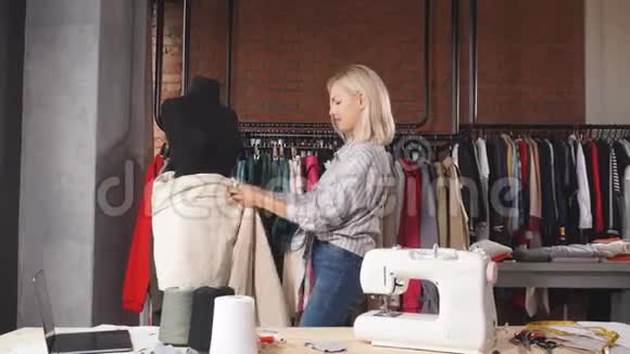 金发美女设计师在工作中测量黑色假人的织物视频的预览图