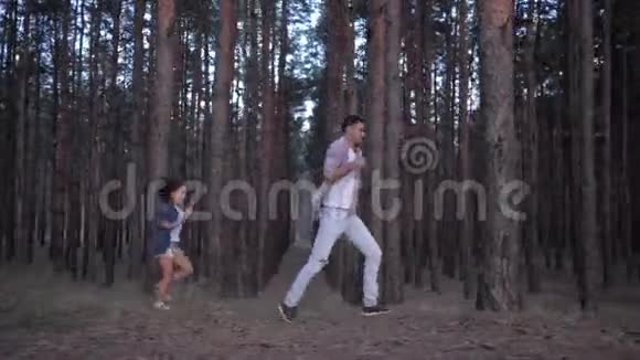 一家人在森林里休息年轻的爸爸玩得很开心在户外的一排排松树之间赶上可爱的女儿视频的预览图