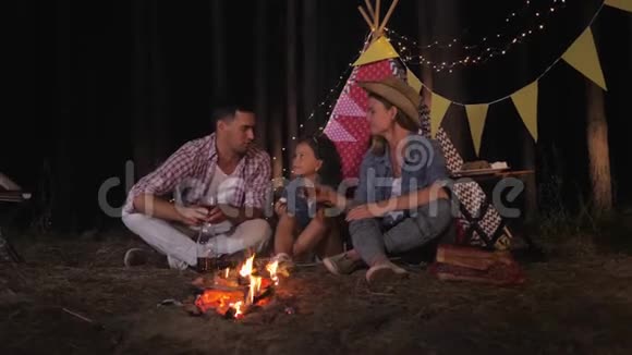 亲爱的亲戚们爸爸妈妈和小女儿在篝火旁的树林里举杯祝酒视频的预览图