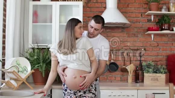 幸福的夫妻正站在厨房里丈夫抚摸怀孕的妻子的肚子视频的预览图