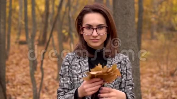 戴眼镜的年轻女子把秋天森林里的黄叶扔在镜头里慢动作视频的预览图