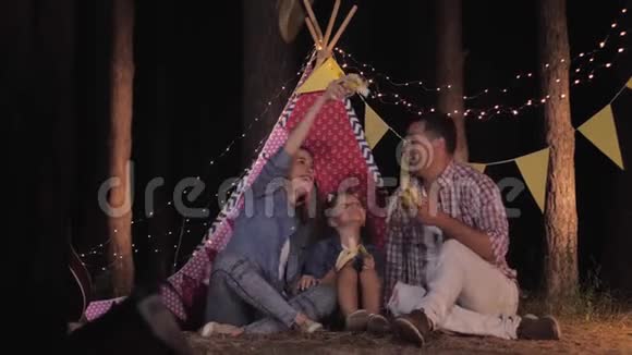 家庭野餐父母和迷人的女儿在森林的背景下吃零食一边吃水果视频的预览图