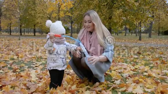 母爱观念妈妈和小女儿在秋天公园吹泡泡视频的预览图